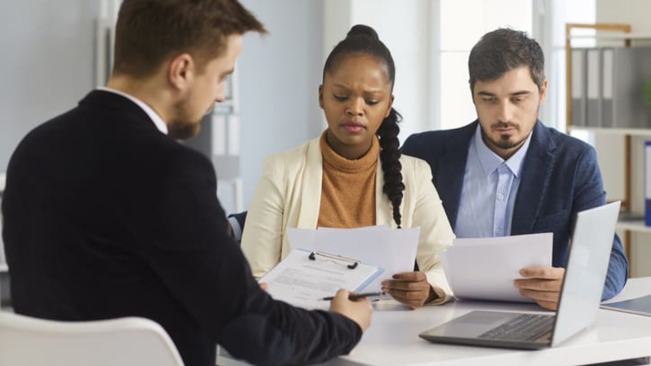 Serious married couple carefully reads paper documents sitting with a bank agent in the office.