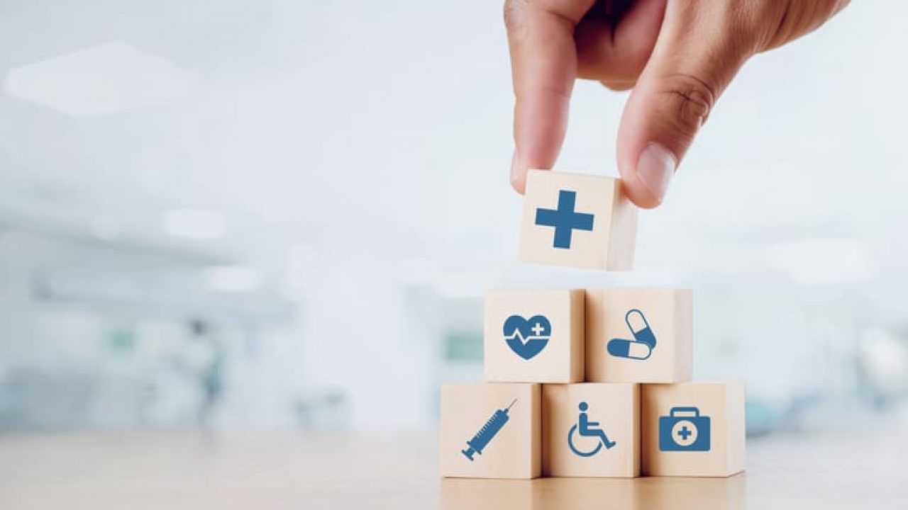 Close up man hand arranging wood block with healthcare medical icon on hospital background. Health care and Health insurance concept.