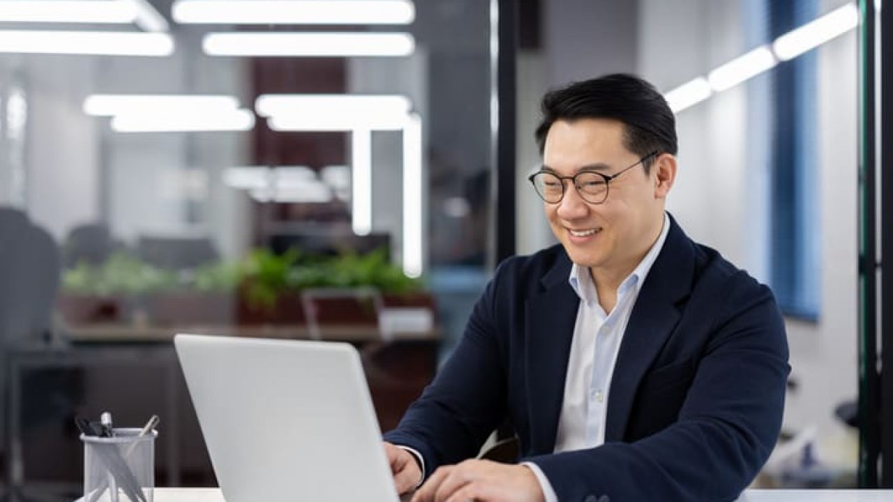 Asian man in business suit and glasses working with laptop inside office, mature businessman typing on keyboard, preparing financial report, male company employee at workplace